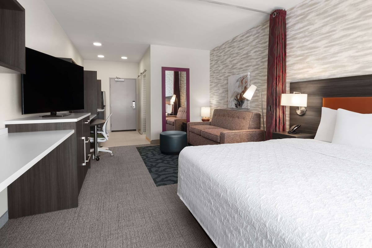 Ett modernt hotellrum med en platt-TV, en soffa, en säng och ett skrivbord med en dator.
