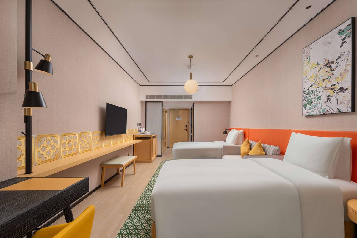 A hotel room with a bed, bedside table, TV, and a desk with a chair.