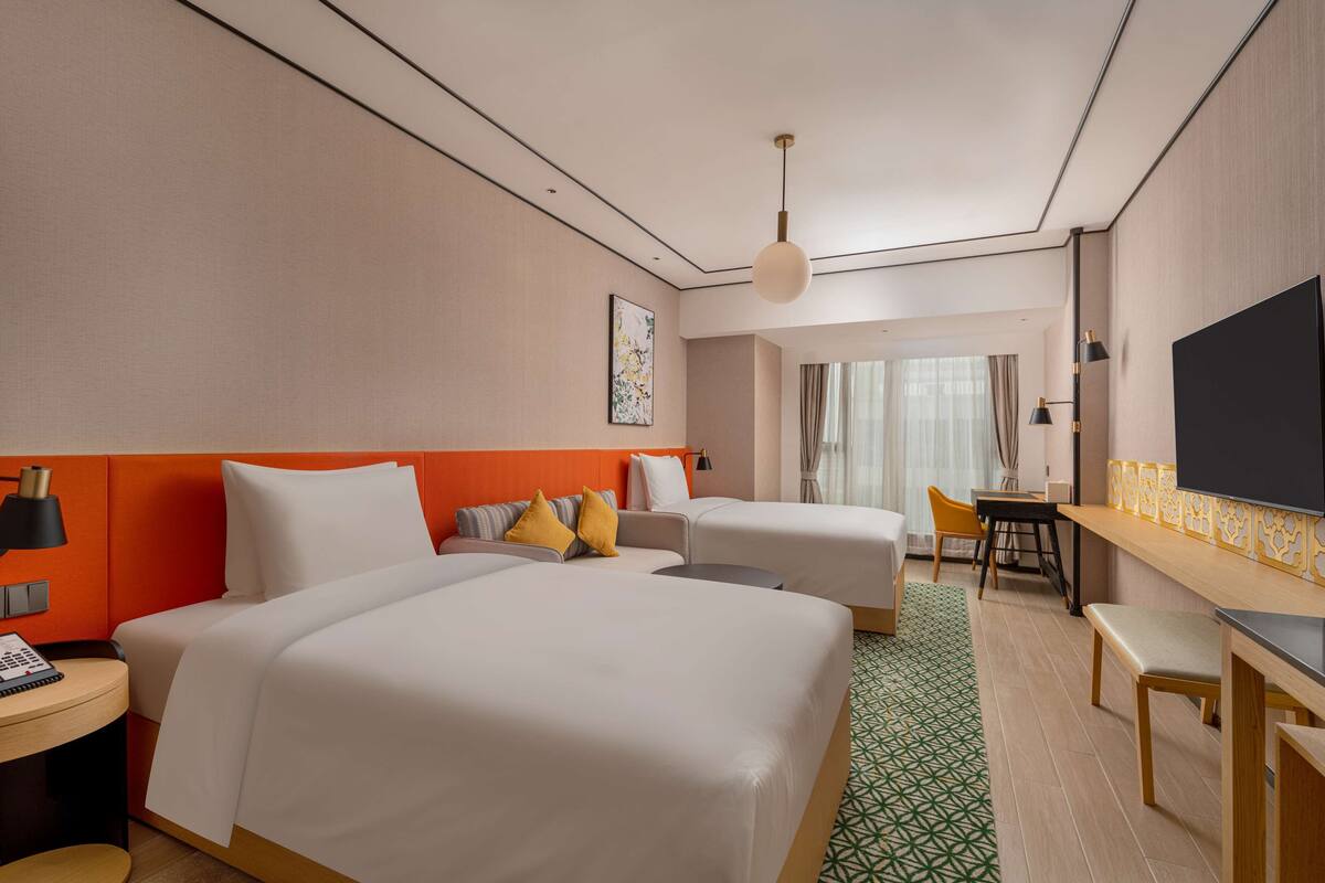 A hotel room with two beds, a desk, a chair, a TV, and a window with curtains.