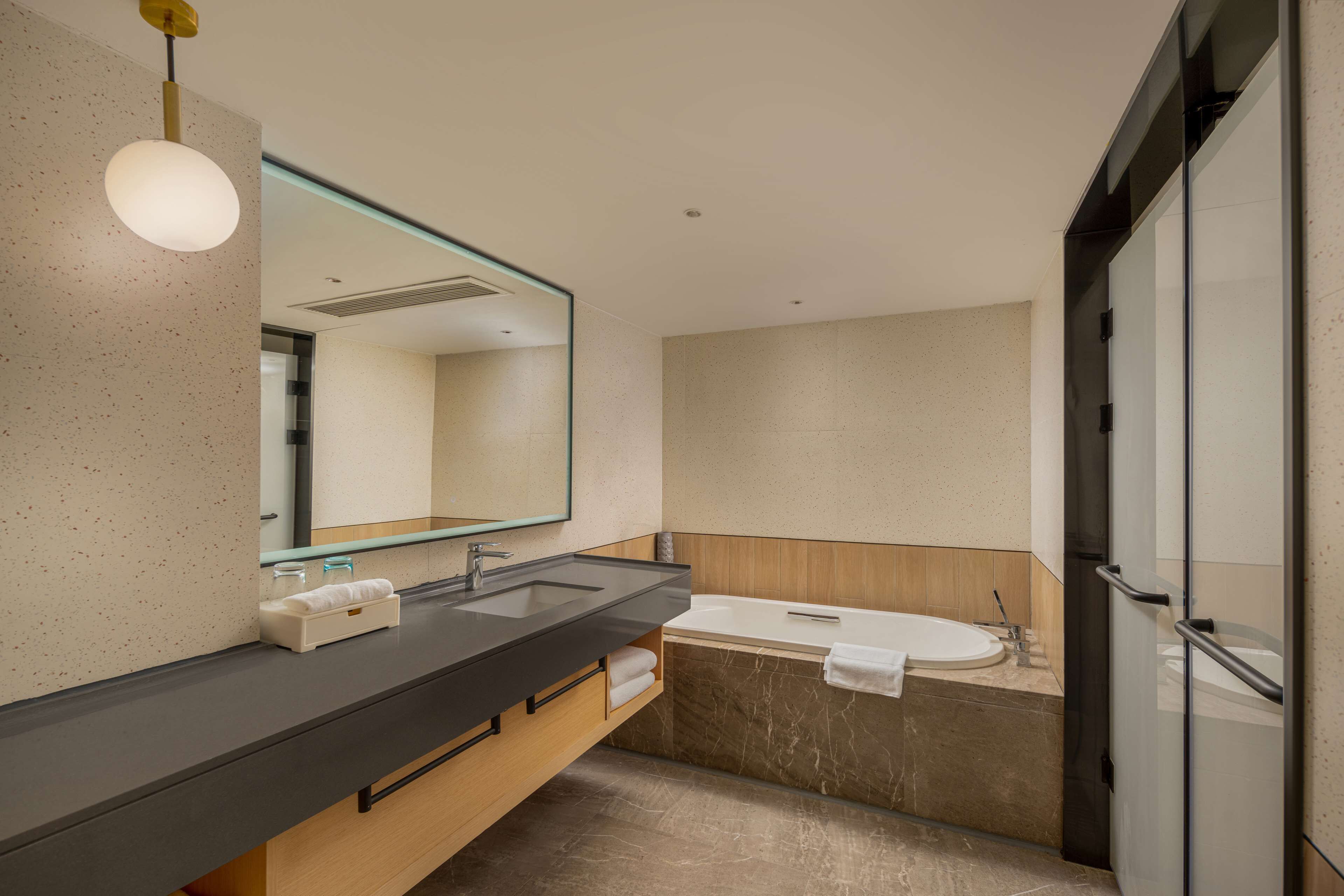 A modern bathroom with a black countertop, a large mirror, a bathtub, and a glass shower enclosure.