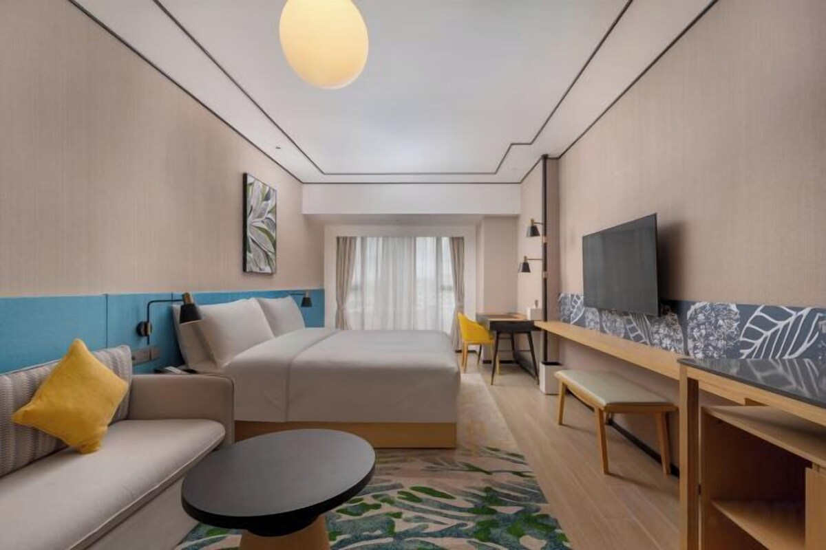 Ett modernt hotellrum med en säng, soffa, skrivbord och tv.