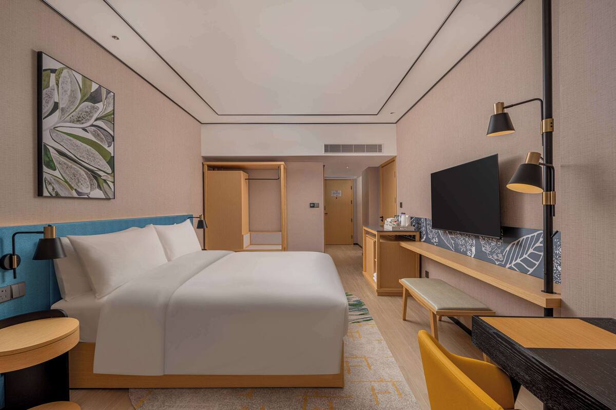 A hotel room with a bed, bedside table, TV, desk, and chair.