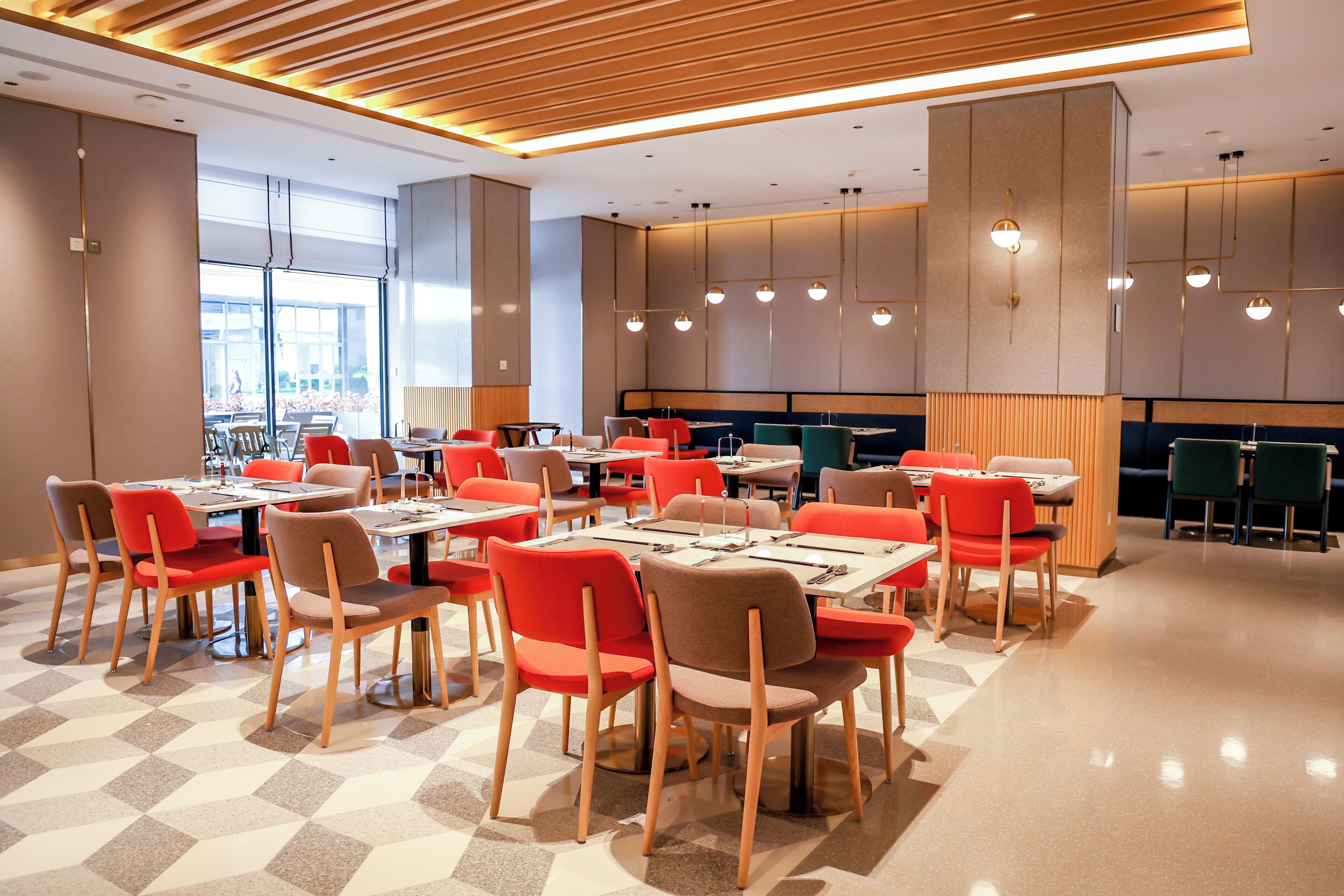 Zona pranzo moderna con diversi tavoli e sedie, ampie finestre e lampade dal design contemporaneo.