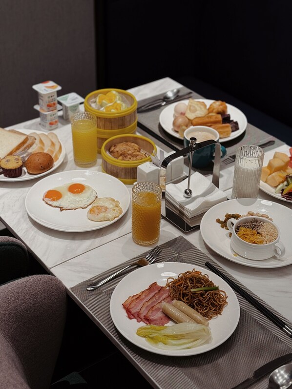 Un buffet de petit-déjeuner proposant divers plats, notamment des œufs, du bacon, des nouilles et des fruits.