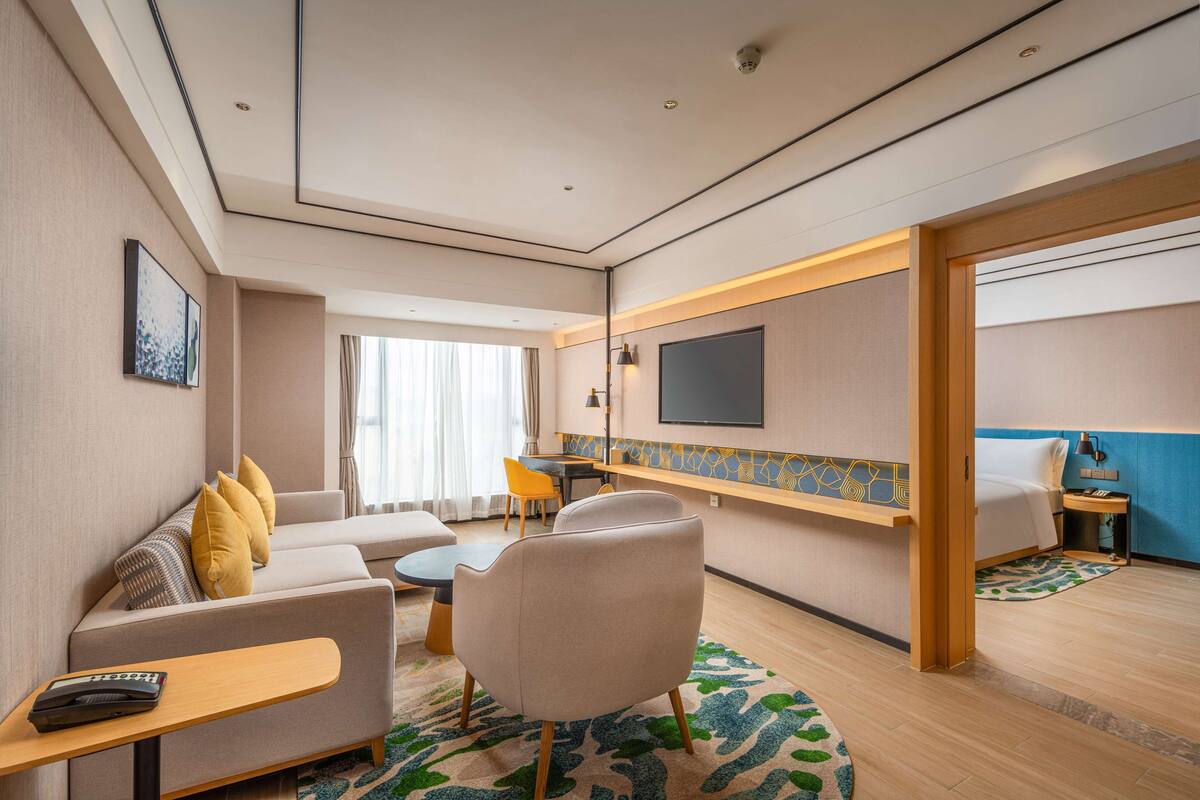 A modern hotel room with a sofa, armchair, and a small table with a remote control.