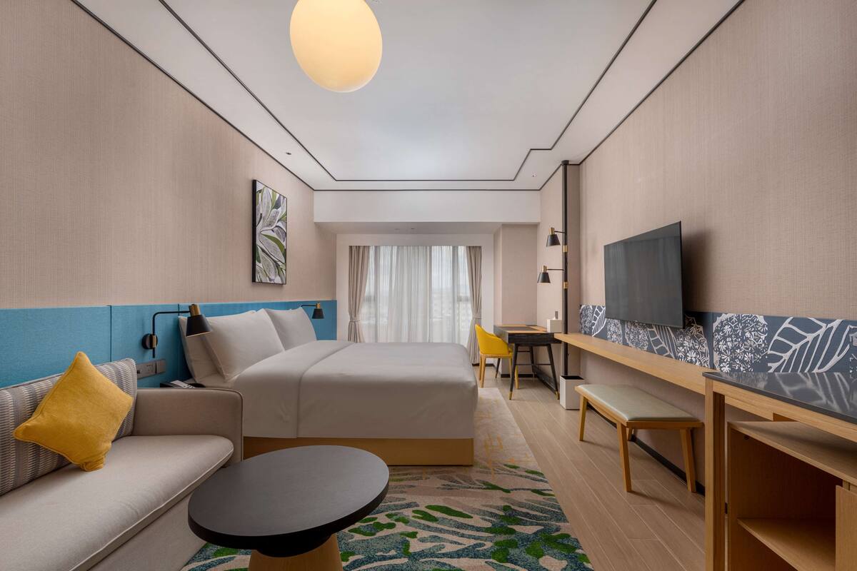A modern hotel room with a bed, sofa, desk, and TV.