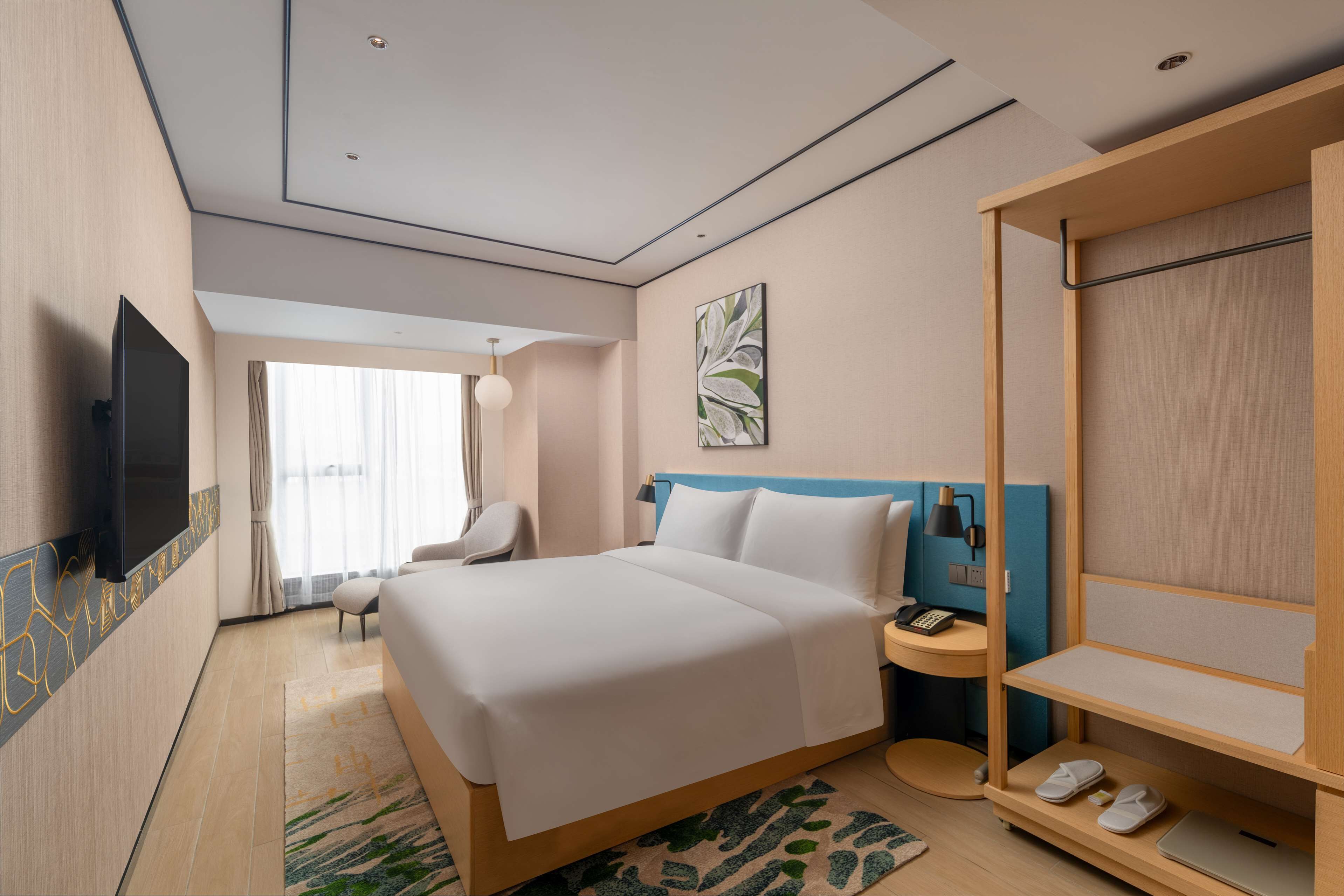 A modern hotel room with a large bed, a flat-screen TV, a desk with a phone, and a wardrobe.