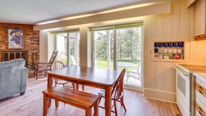A dining area with a wooden table and chairs, a fireplace, and a view of the outdoors through large sliding glass doors. - Ski-In/Ski-Out Bromley Mtn Condo: Wood Fireplace! (Peru)