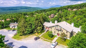 A large, two-story building with a flat roof and a red door, surrounded by lush greenery and a parking area with several cars. - Ski-In/Ski-Out Bromley Mtn Condo: Wood Fireplace! (Peru)