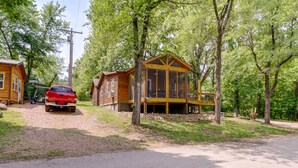 Una cabaña de madera con un ventanal grande y un porche, rodeada de árboles.