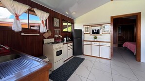 Een kleine keuken met een spoelbak, fornuis, koelkast en kastjes.