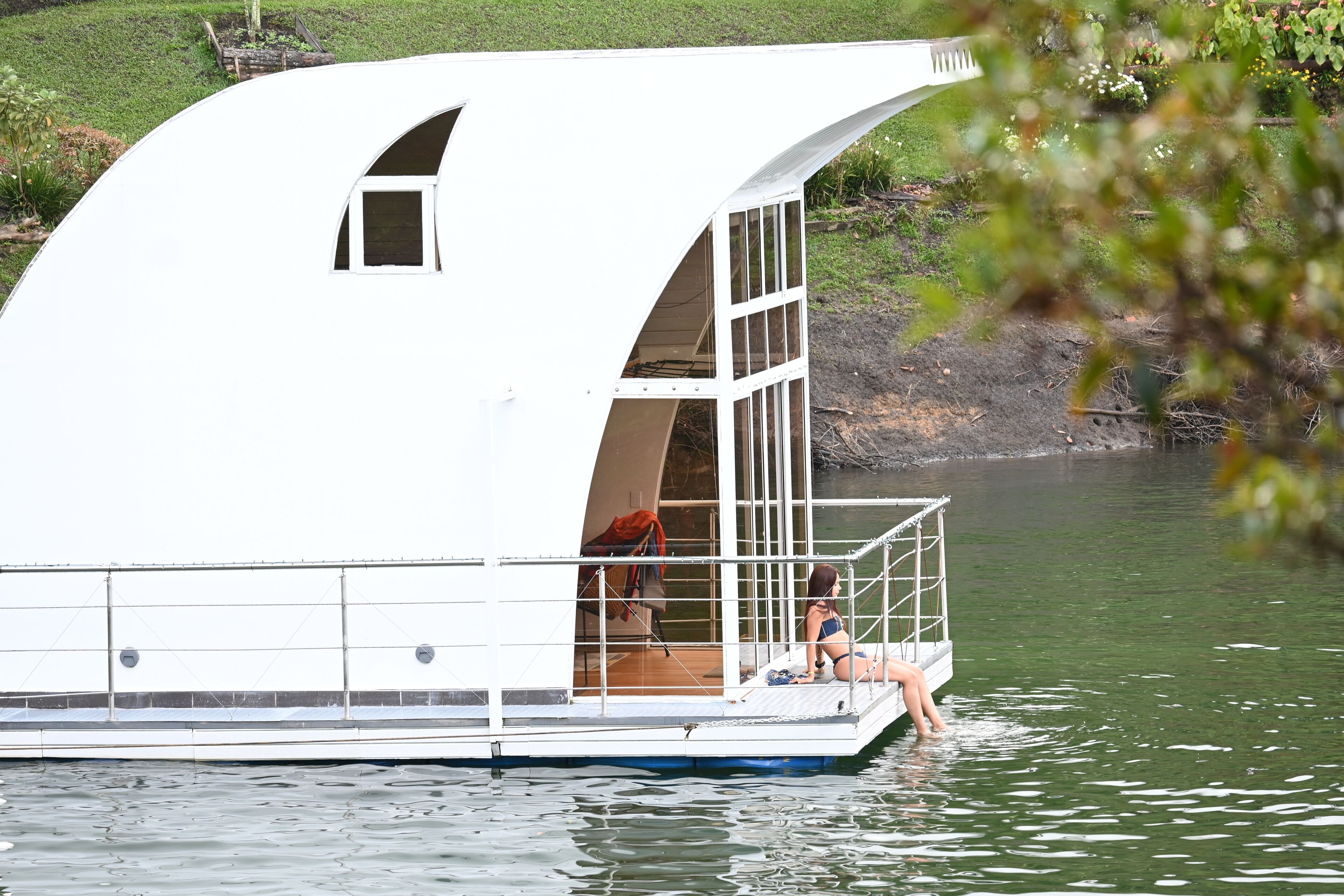 A houseboat with a large open deck and a small window, situated on a calm body of water.
