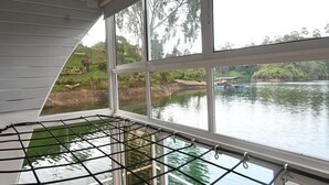 A room with large windows overlooking a lake, a hammock, and a view of the surrounding greenery. - La trinidad (Guatapé)