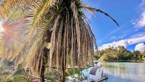 A serene lakeside setting with a wooden deck, a white building, and lush greenery. - La trinidad (Guatapé)