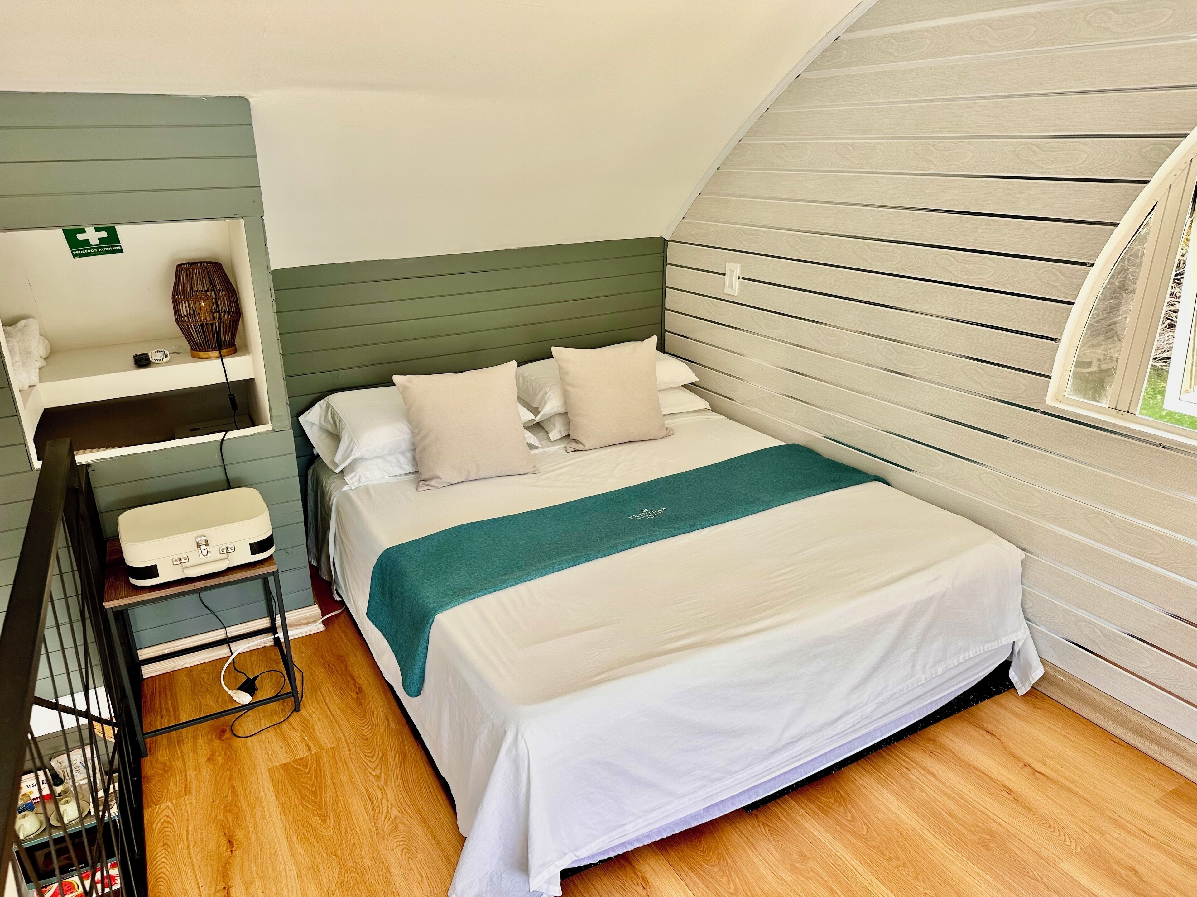 A neatly arranged bedroom with a bed, bedside table, and a shelf with a first aid kit.