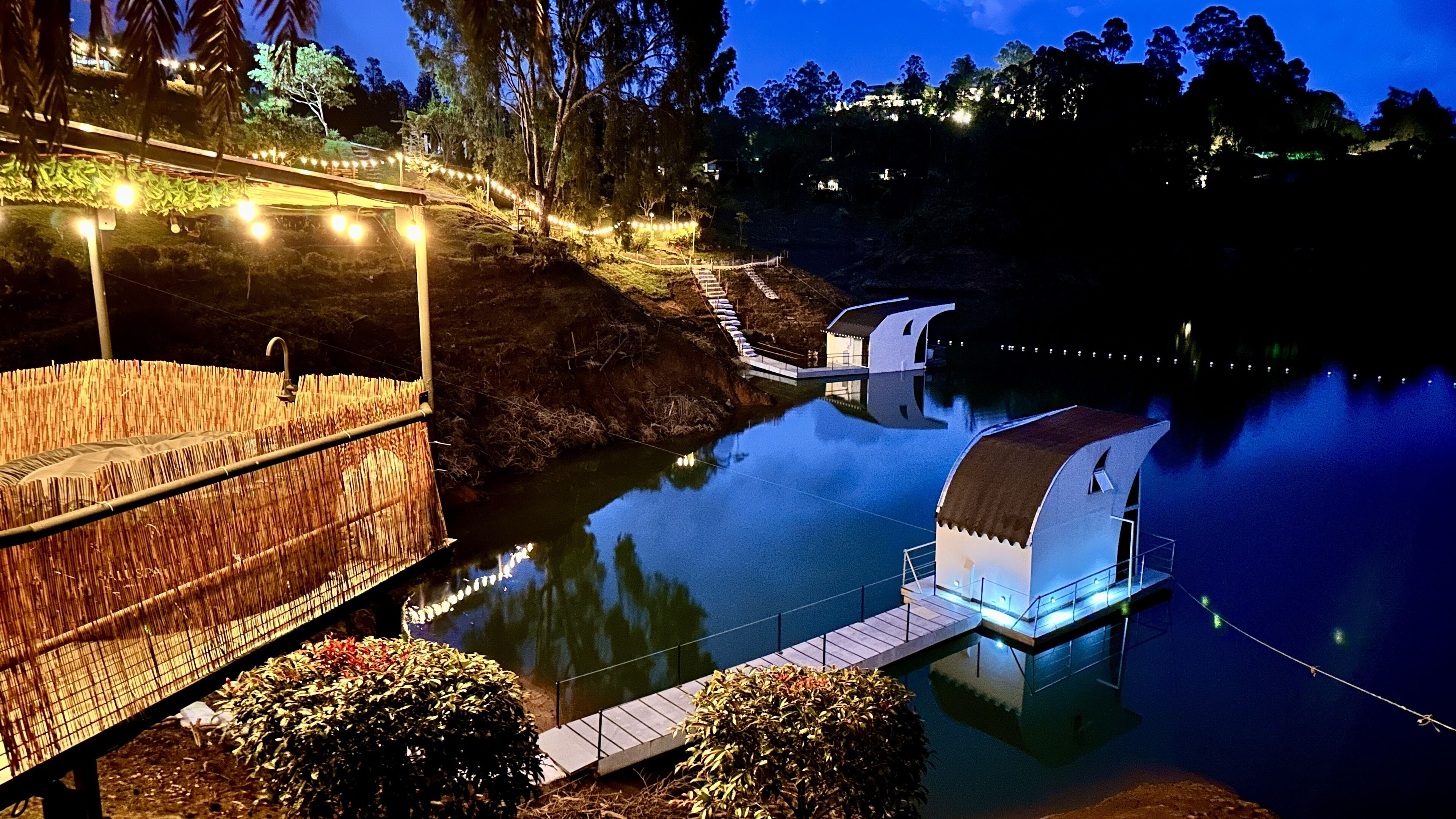 Un hotel frente al agua con una terraza cubierta, un pequeño embarcadero y un reflejo en el agua.