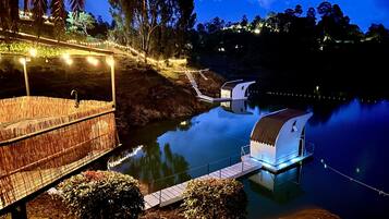 Un hotel frente al agua con una terraza cubierta, un pequeño embarcadero y un reflejo en el agua.