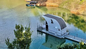 A floating house with a modern design, situated on a calm lake surrounded by greenery. - La trinidad (Guatapé)