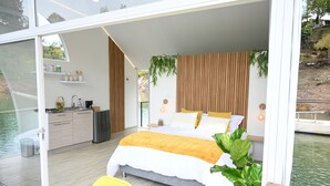 A modern bedroom with a large bed, wooden paneling, and a view of a water body. - La trinidad (Guatapé)