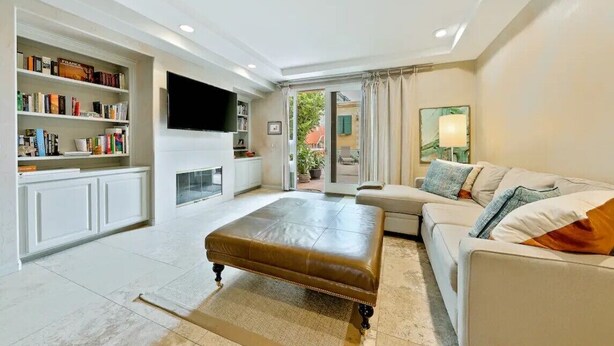 A modern living room with a leather ottoman, a sofa, a flat-screen TV, a bookshelf, and a fireplace. - Walk to Village/Beach/A/C/EV Charger/Parking (La Jolla)