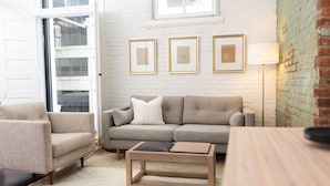 Un salon comprenant un canapé, un fauteuil, une table basse et une lampe. Trois tableaux encadrés ornent le mur.
