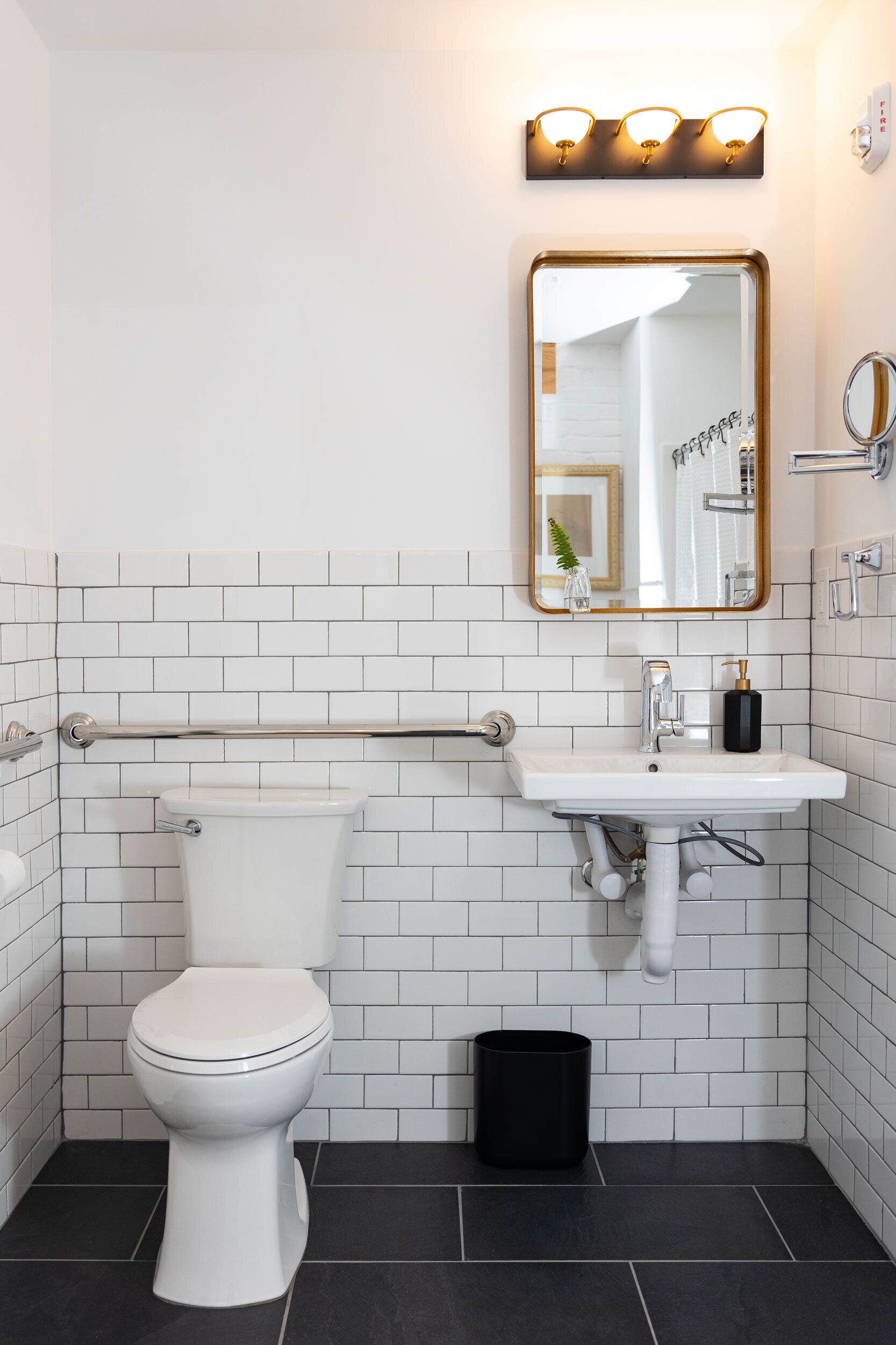 Een badkamer met een wit toilet, een wastafel met spiegel erboven en een zwarte prullenbak.