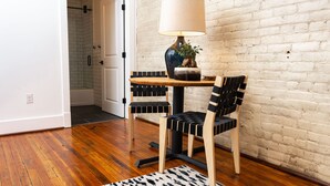 Une pièce avec un plancher en bois, un tapis à motifs noir et blanc, une table avec une lampe et une plante, et deux chaises à rayures noires et blanches.