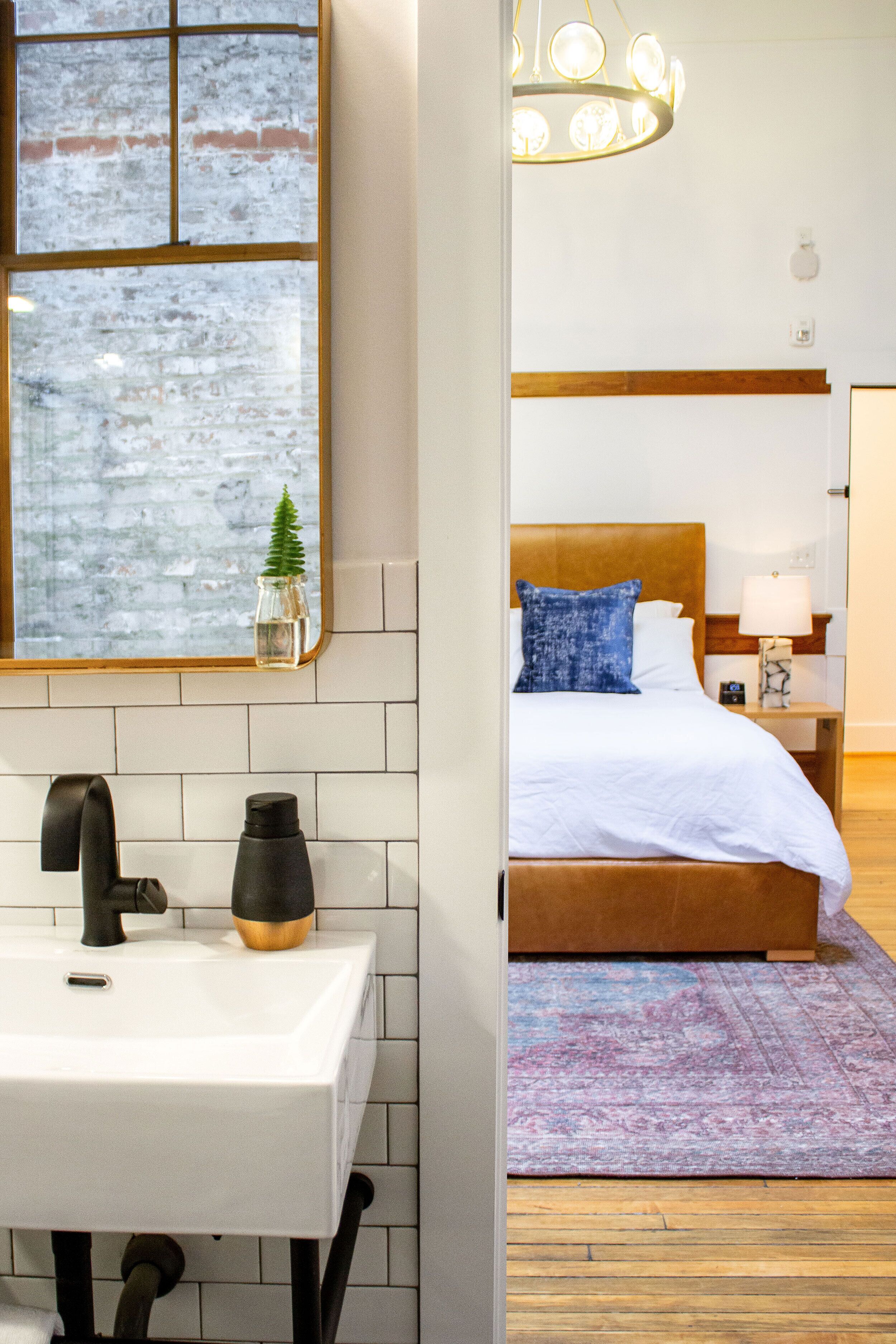 A bathroom with a white sink, a mirror, and a window with a view of a brick wall.