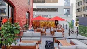 Un espace extérieur aménagé avec des tables et des chaises, des parasols rouges et un bâtiment en briques en arrière-plan.
