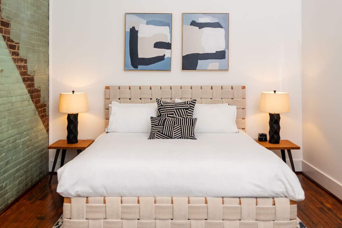 Ein Schlafzimmer mit einem Bett, zwei Nachttischen, einer Hängeleuchte und abstrakten Wandbildern.