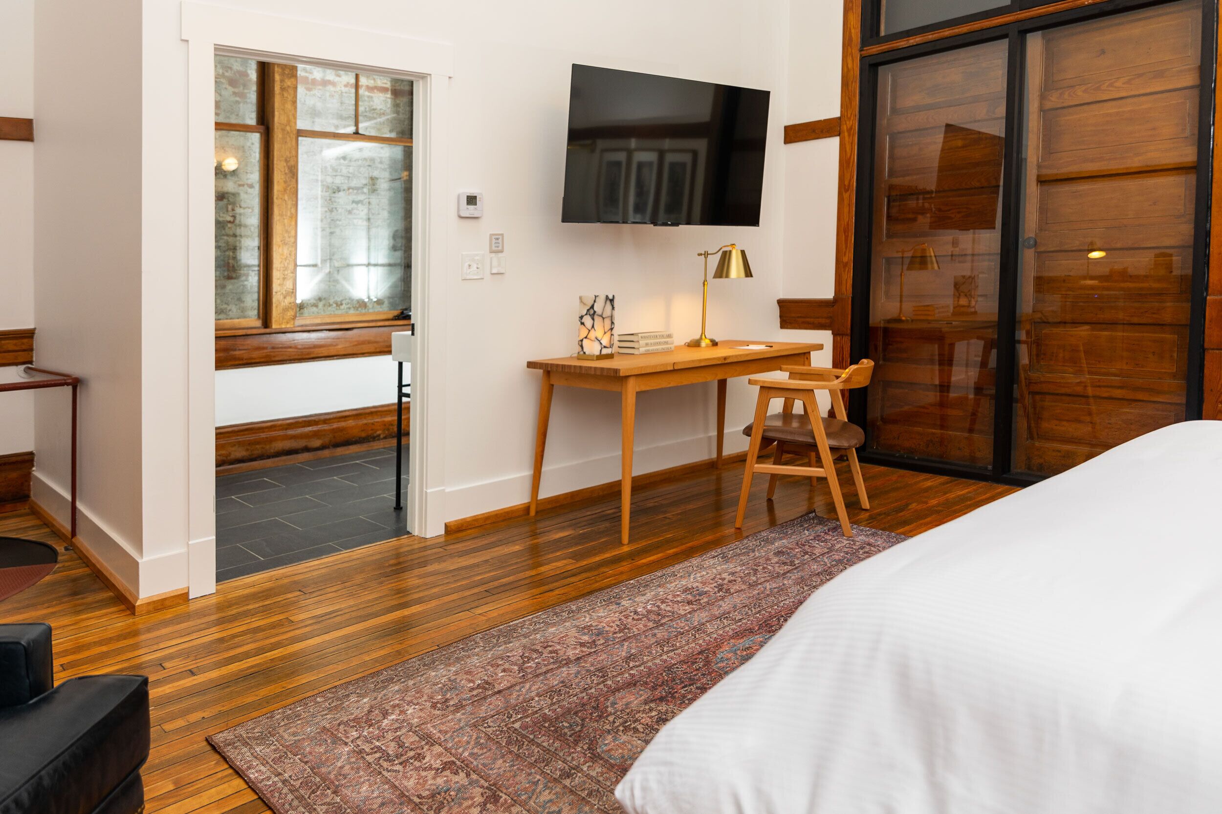 Un dormitorio moderno con una cama grande, un escritorio con silla, un televisor y un ventanal amplio.