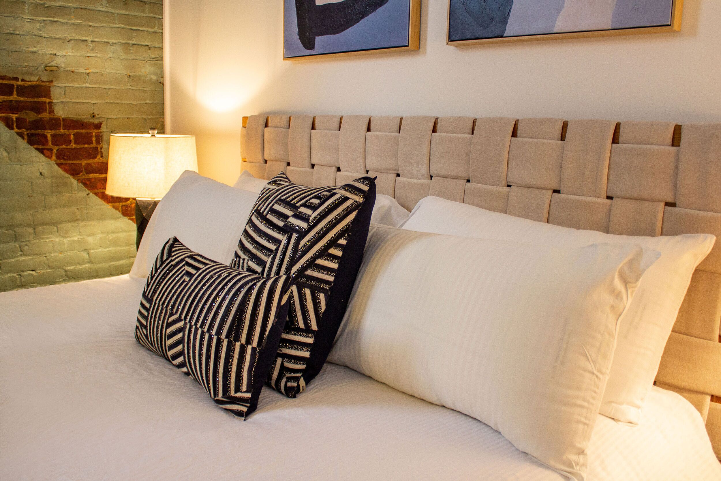Un lit bien fait, avec une tête de lit capitonnée, un coussin à rayures et un coussin uni.