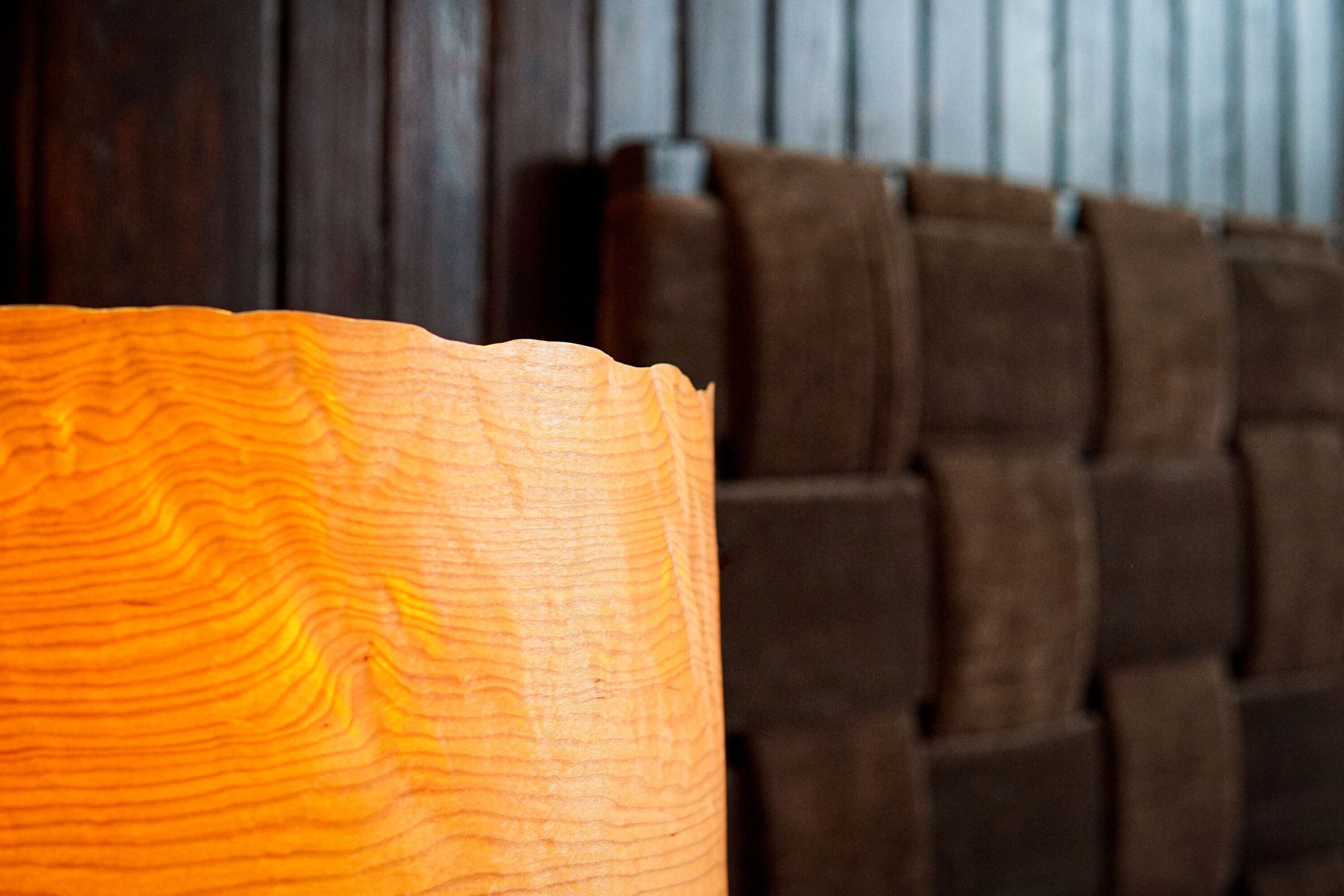 A close-up of a wooden object with a wavy pattern, likely a part of furniture, in a room with a dark wooden wall and a brown upholstered headboard.