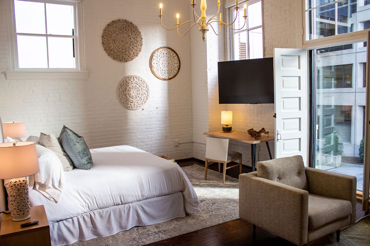 Ein Schlafzimmer mit Bett, Nachttisch, Lampe, Stuhl, Schreibtisch, Fernseher und Wanddekoration.