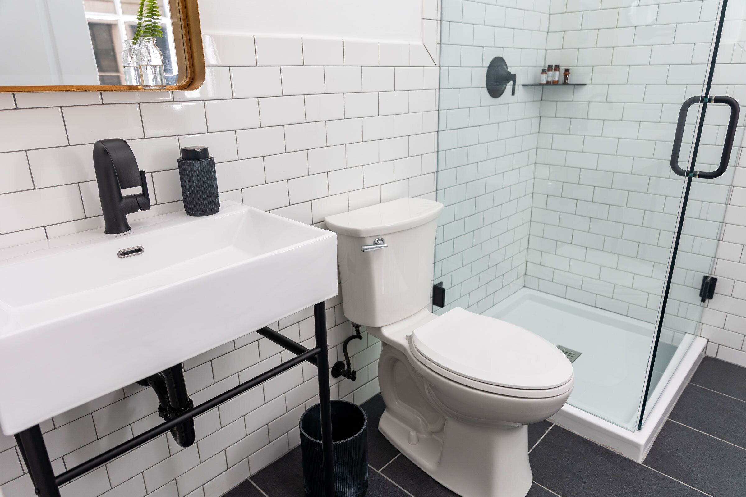 A modern bathroom with a white sink, black faucet, and a glass shower enclosure.