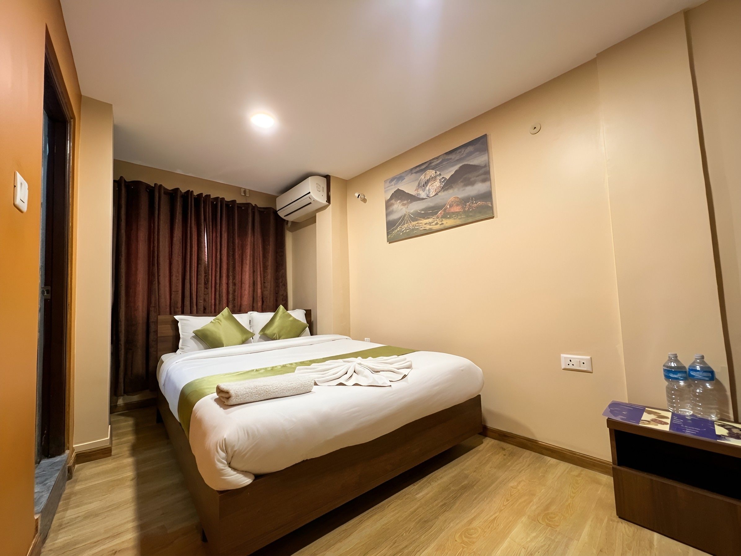 Una habitació d'hotel amb un llit, un quadre a la paret i una ampolla d'aigua a la tauleta de nit.