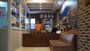 A reception area with a wooden desk, a brown couch, and a wall decorated with posters and a mural. - Holiday Hostel (Kathmandu)