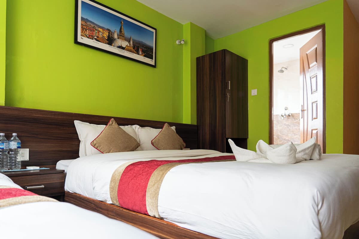 A hotel room with a large bed, a wooden headboard, a green wall, and a framed picture above the bed.