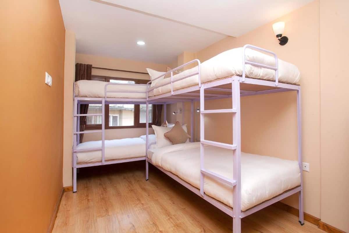 A room with three bunk beds, wooden flooring, a window with curtains, and a wall-mounted light fixture.