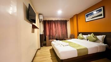 A hotel room with a bed, a desk, a chair, a television, and a painting on the wall.