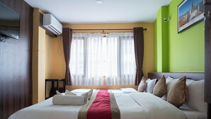 A hotel room with a large bed, a flat-screen TV, an air conditioning unit, and a window with curtains. - Holiday Hostel (Kathmandu)