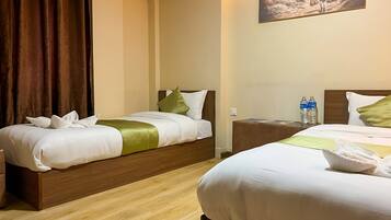 A hotel room with two beds, wooden headboards, a painting on the wall, and a nightstand with water bottles.