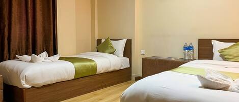 A hotel room with two beds, wooden headboards, a painting on the wall, and a nightstand with water bottles.