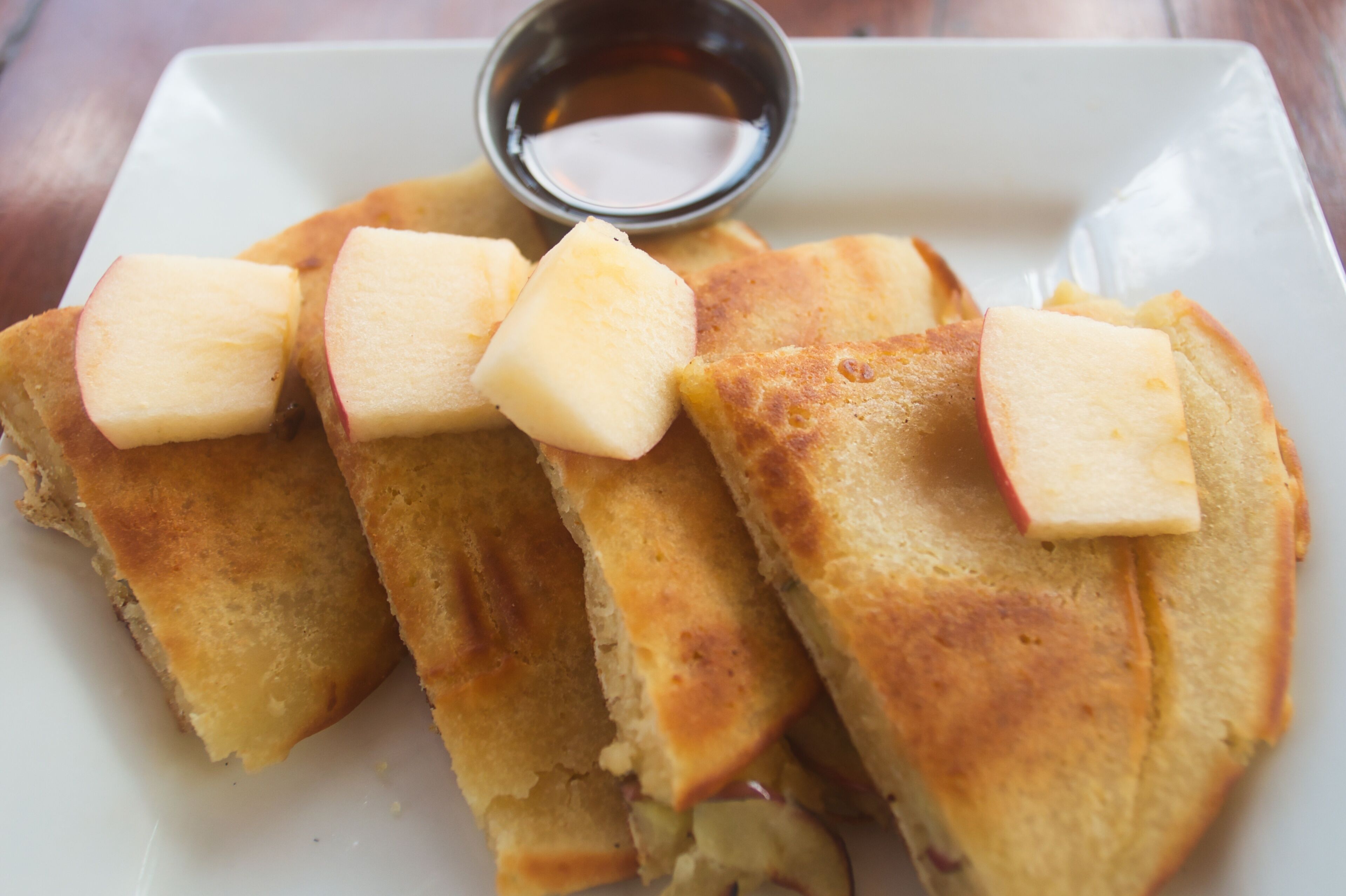 A plate of grilled cheese sandwiches with apple slices on top and a small bowl of sauce.