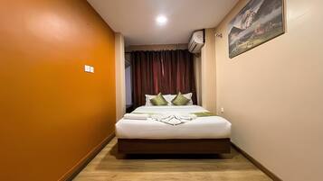 A hotel room with a bed, a painting on the wall, and an air conditioning unit.