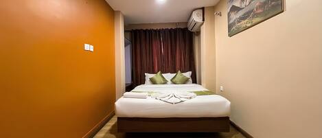 A hotel room with a bed, a painting on the wall, and an air conditioning unit.
