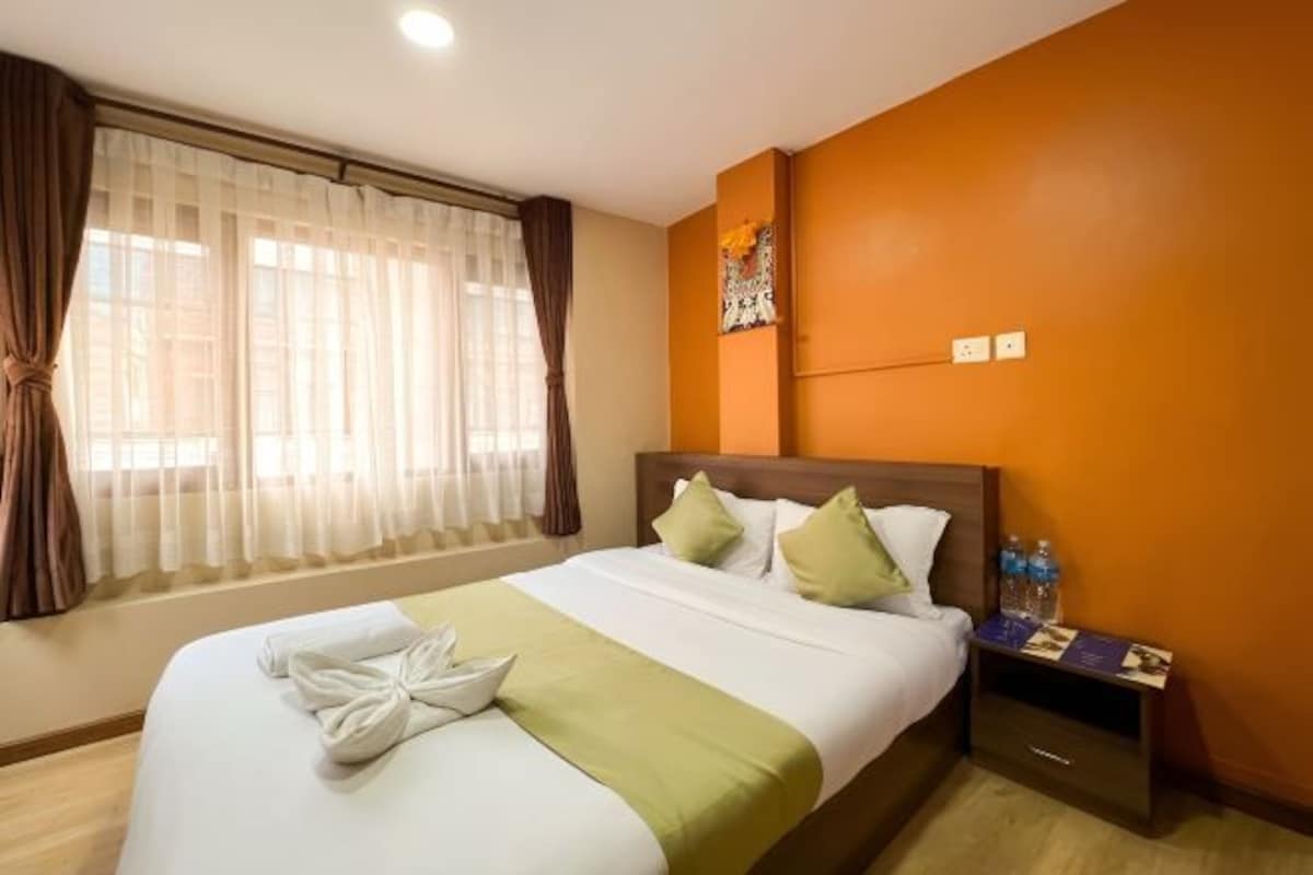 A hotel room with a bed, curtains, a nightstand, and a wall-mounted artwork.
