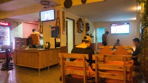 A restaurant with wooden furniture, a Coca-Cola refrigerator, and televisions on the walls. - Holiday Hostel (Kathmandu)