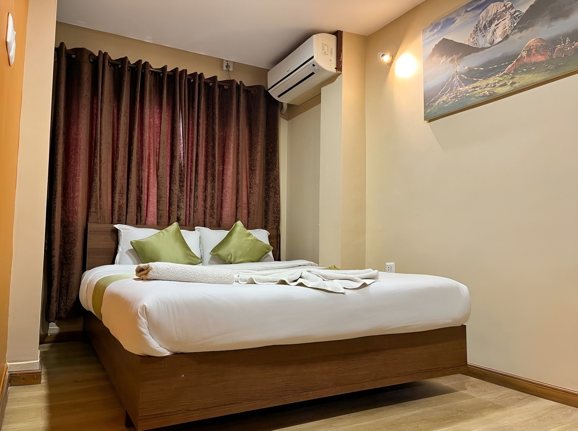 A hotel room with a bed, a painting on the wall, and an air conditioning unit.