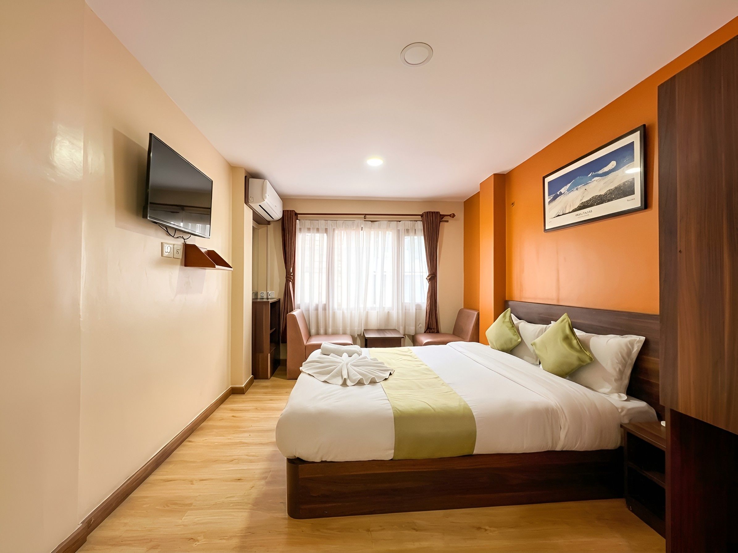 A hotel room with a bed, a television, a window with curtains, and a framed picture on the wall.